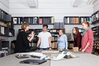 Dieses Bild zeigt eine Professorin und eine Gruppe von Studierenden im Materiallager des Fachbereichs Architektur der Peter Behrens School of Arts.